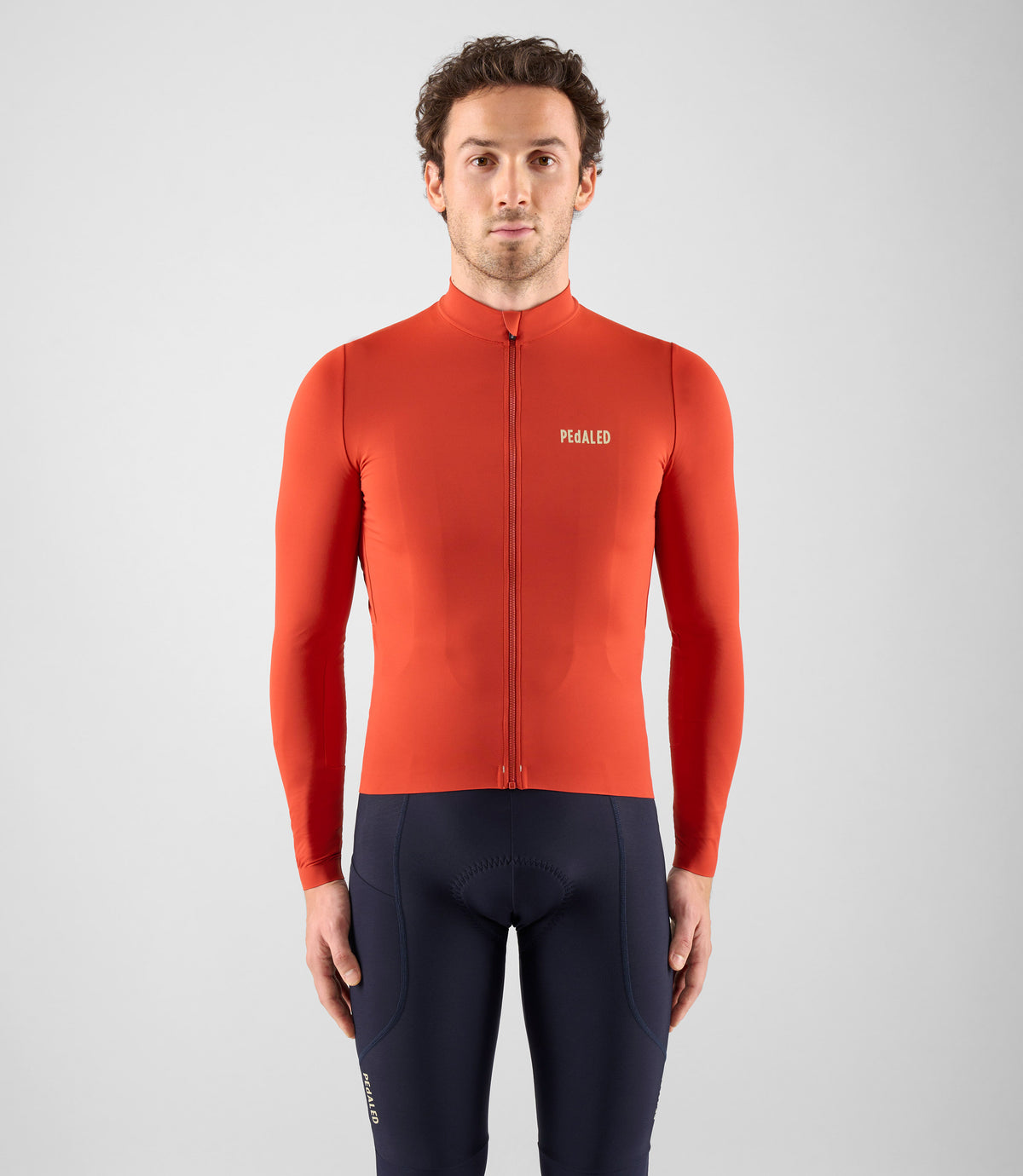 Model wearing a vivid red PEdALED long-sleeve cycling jersey with dark bib shorts